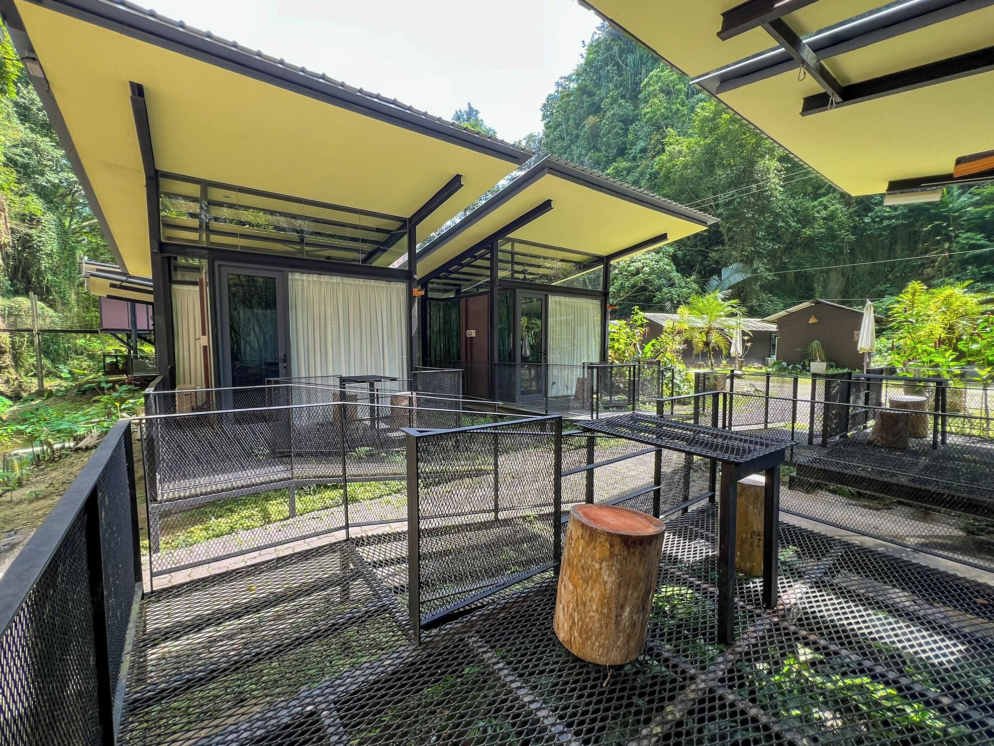 A modern outdoor area with a yellow roof, metal mesh flooring, and a wooden stump.