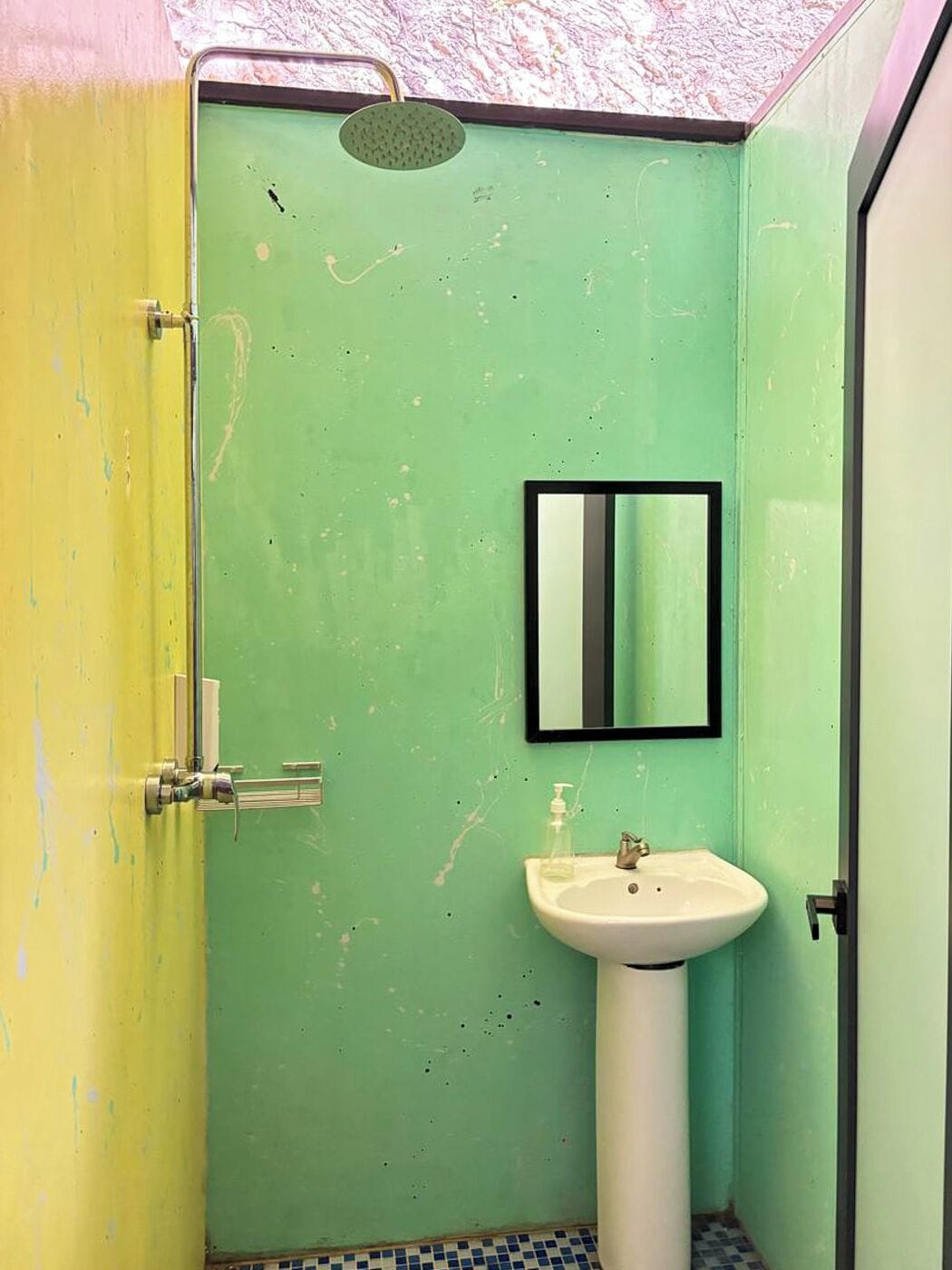 A bathroom with a green wall, a yellow door, a white sink, and a shower.