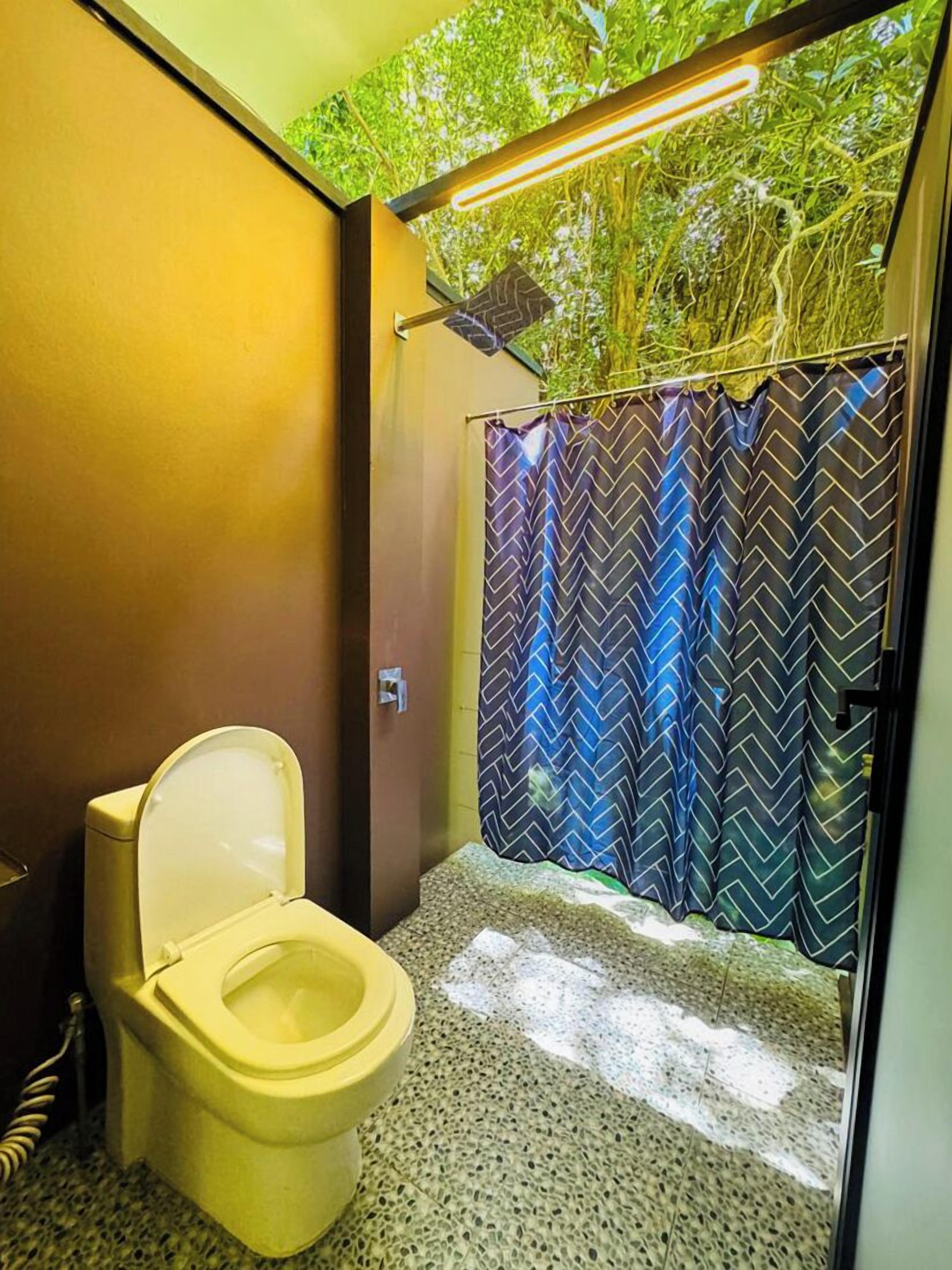 A bathroom with a toilet, a shower curtain with a chevron pattern, and a green artificial plant wall.