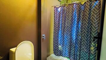 A bathroom with a toilet, a shower curtain with a chevron pattern, and a green artificial plant wall.