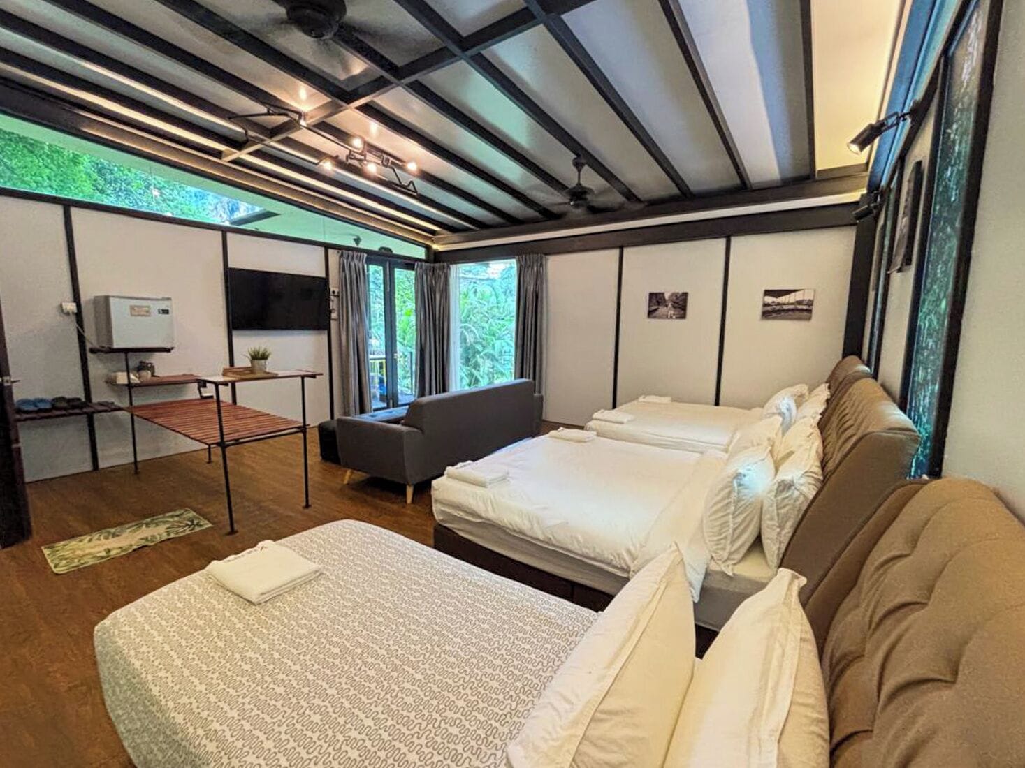 A modern hotel room with two beds, a sofa, a small table, and a TV.