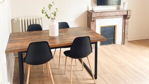 A dining area with a wooden table, black chairs, a white vase with plants, a fireplace, and a TV on a mantel. - L'Angevin-4 pers-espace repas-Centre ville/Gare station (Le Mans)