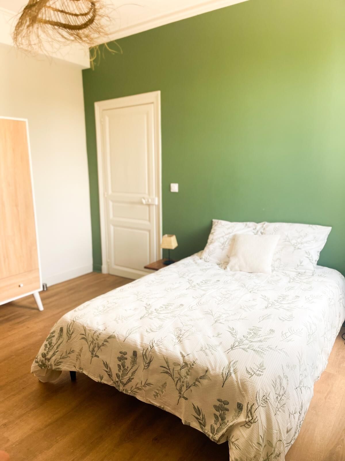 Un dormitorio con cama, puerta y suelo de madera.