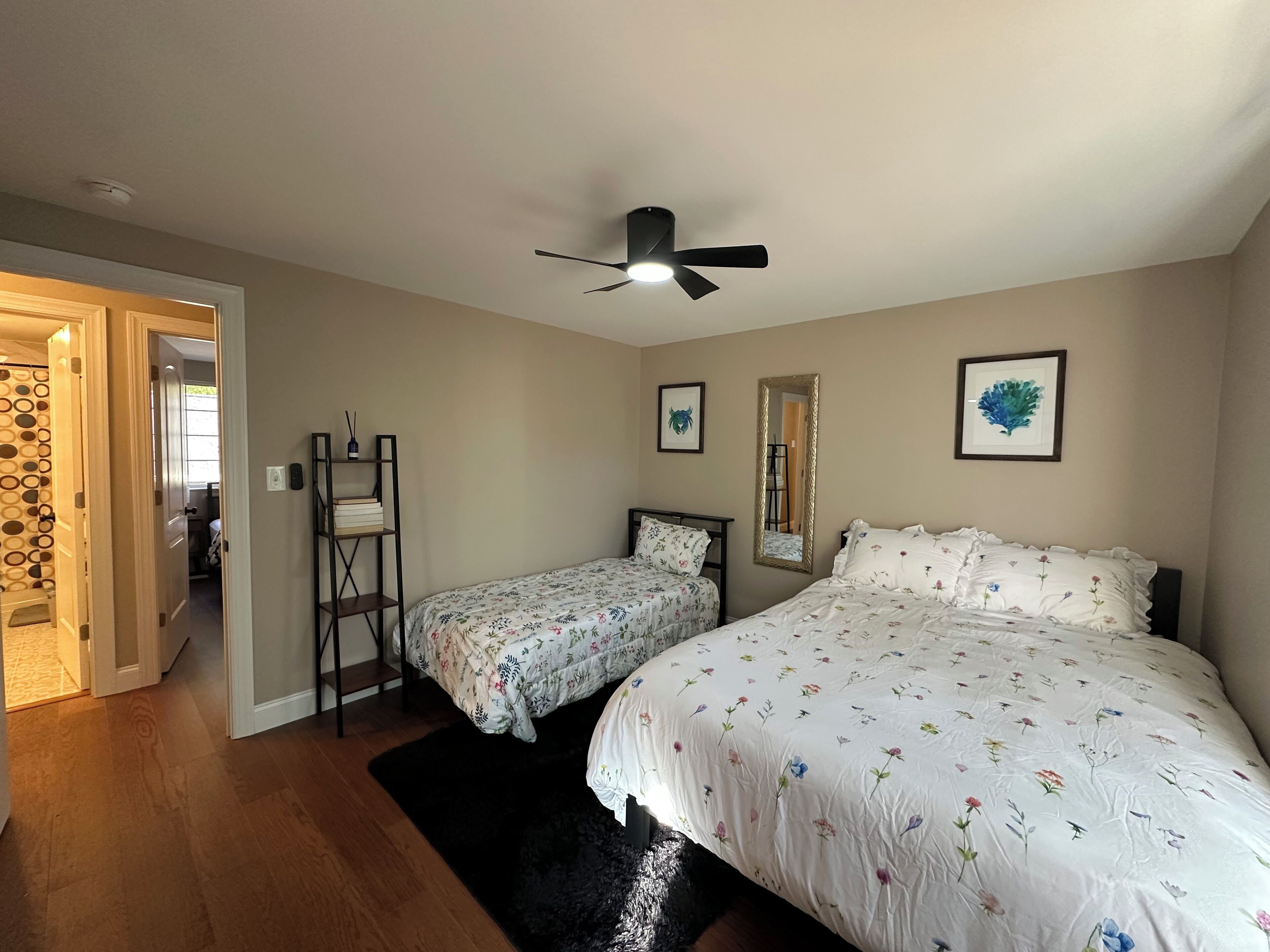 A bedroom with two beds, a ceiling fan, a bookshelf, and a mirror.
