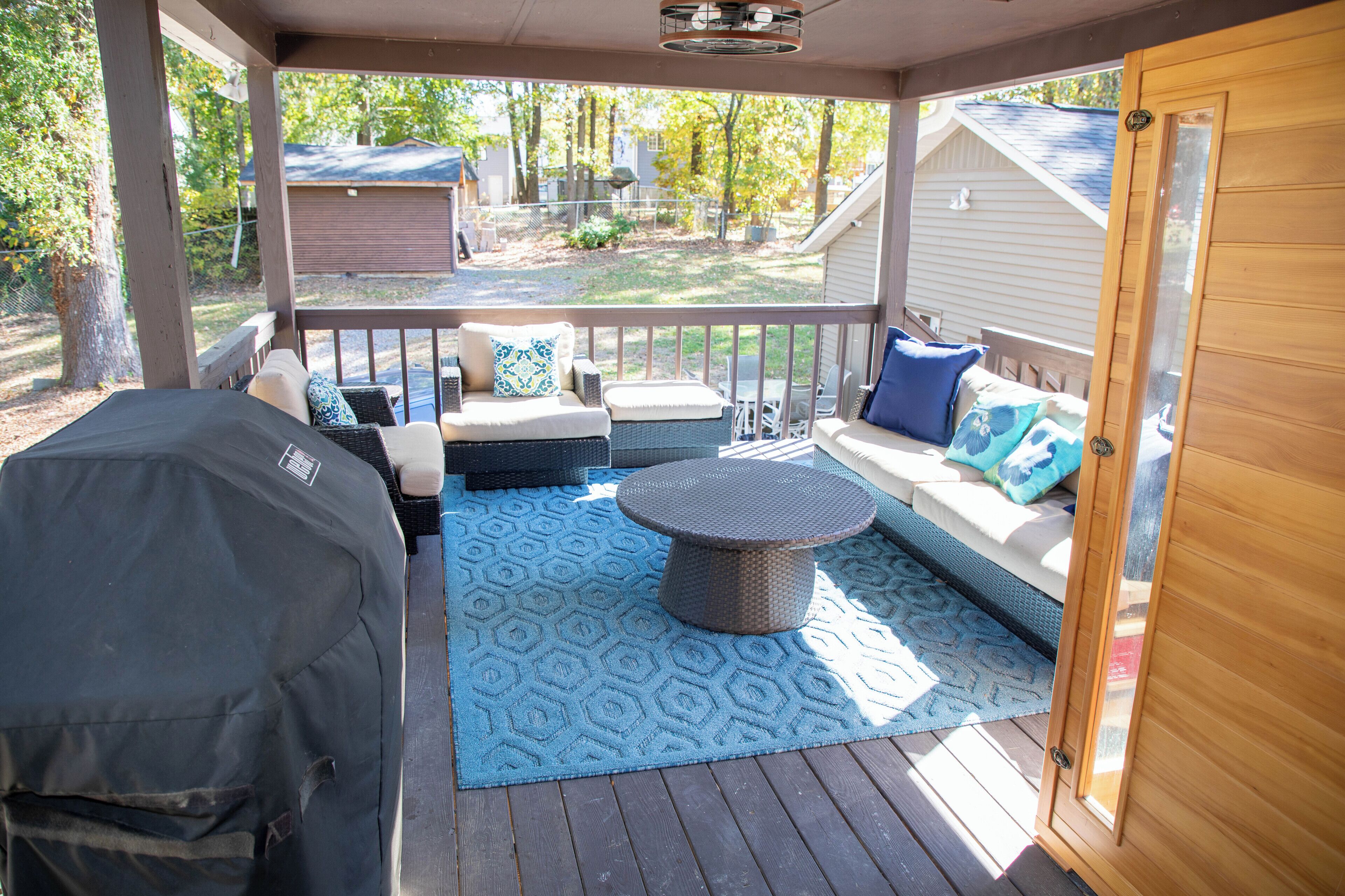 A covered outdoor seating area with a sofa, cushions, and a round table.
