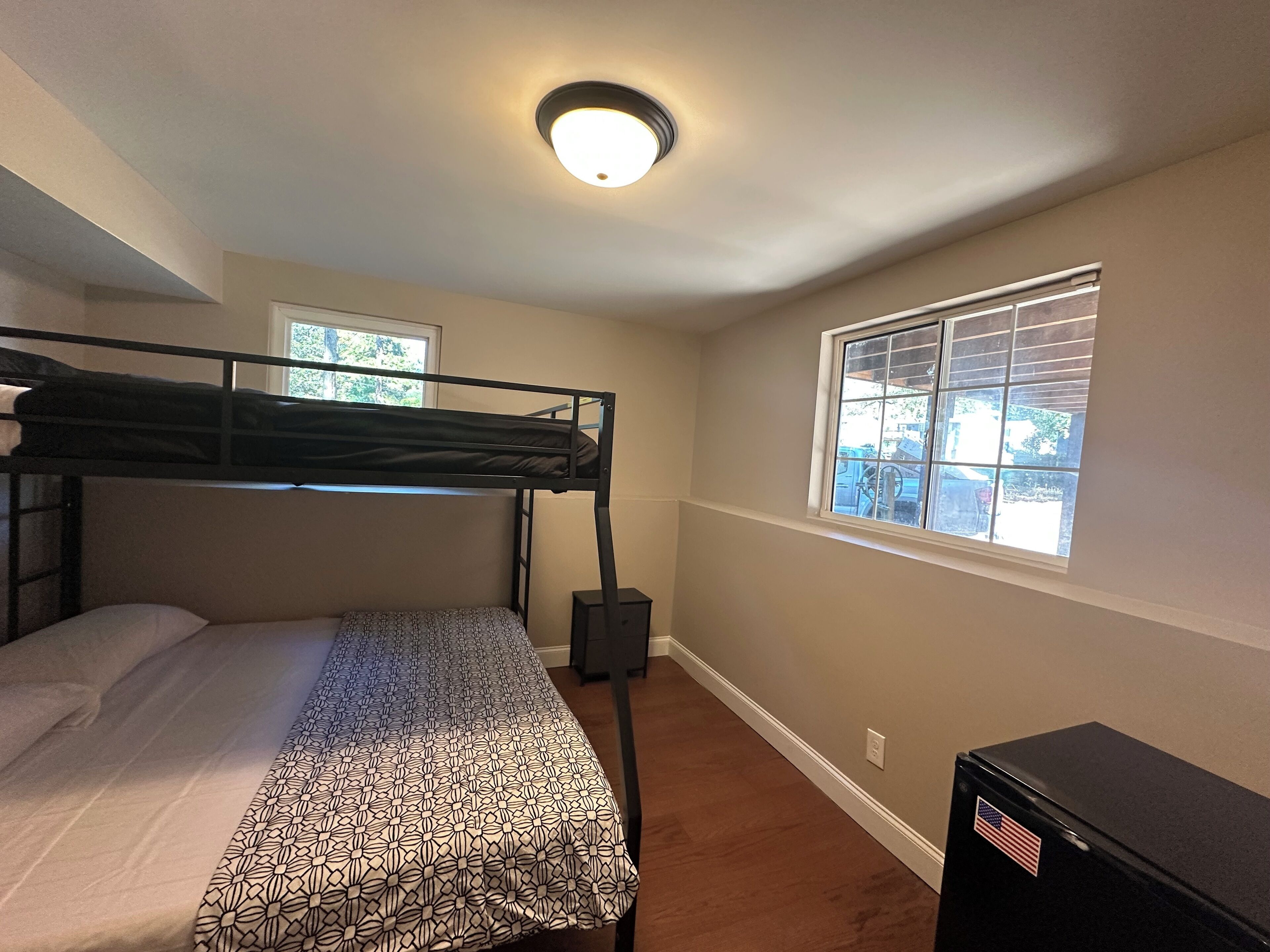 A bunk bed room with a window, a ceiling light, and a small black cabinet.