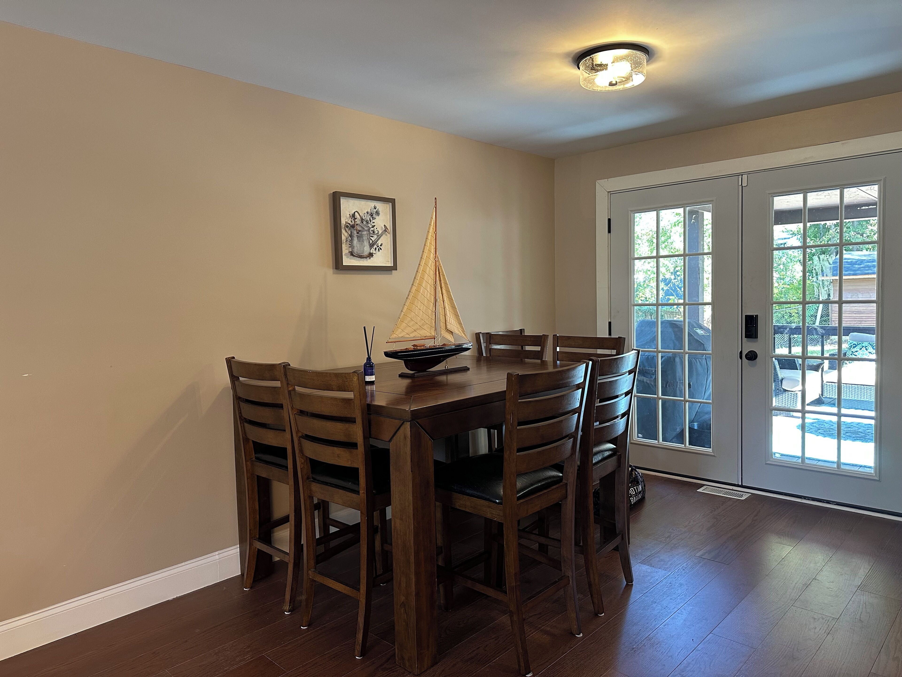 A dining area with a wooden table and chairs, a sailboat model, and a door leading outside.