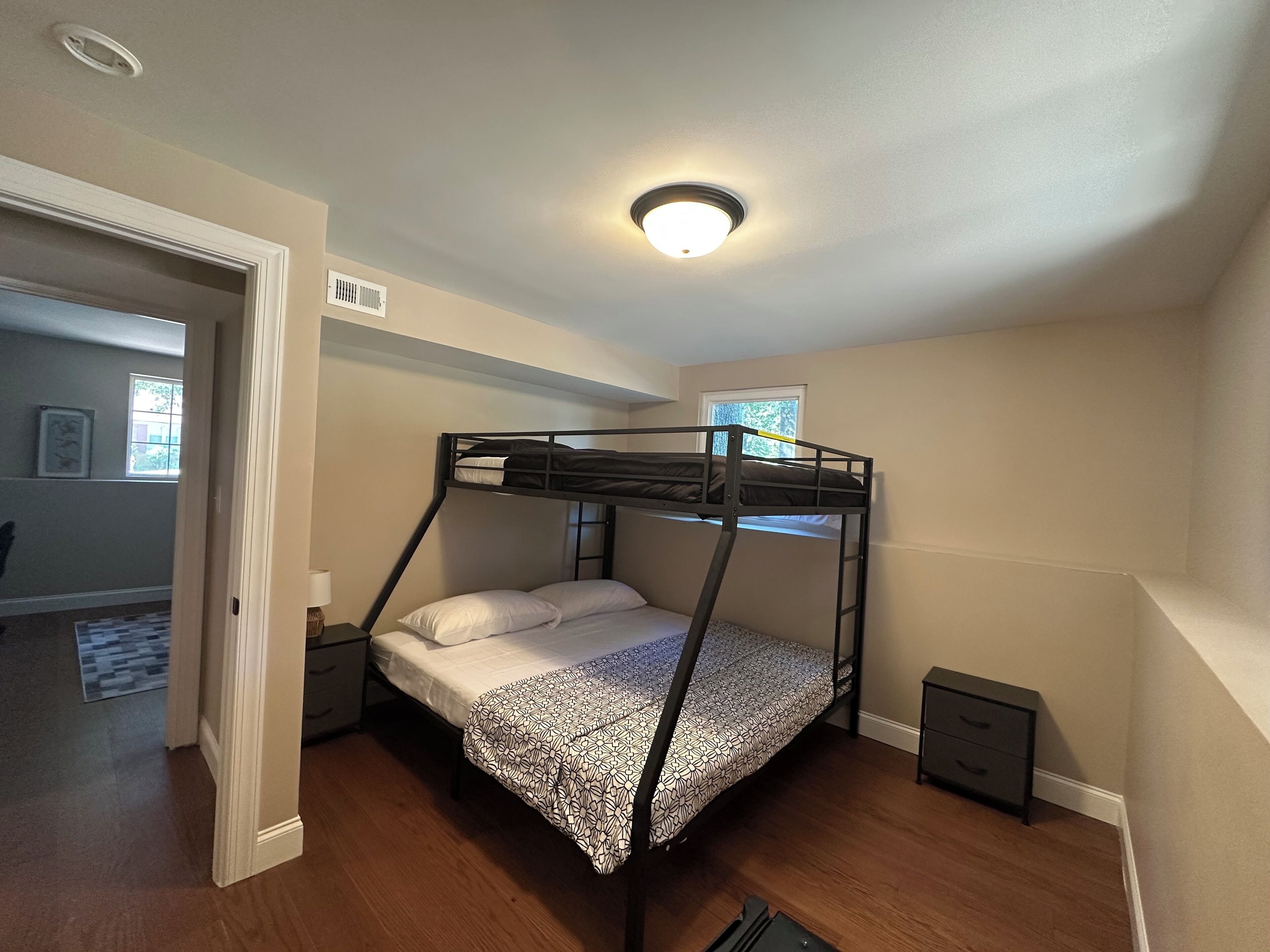 Una cama litera en una habitación con luz en el techo, una ventana y una puerta que da a otra habitación.