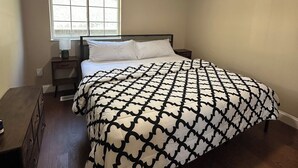 Un dormitorio con cama, mesita de noche, cómoda, ventana y ventilador de techo.