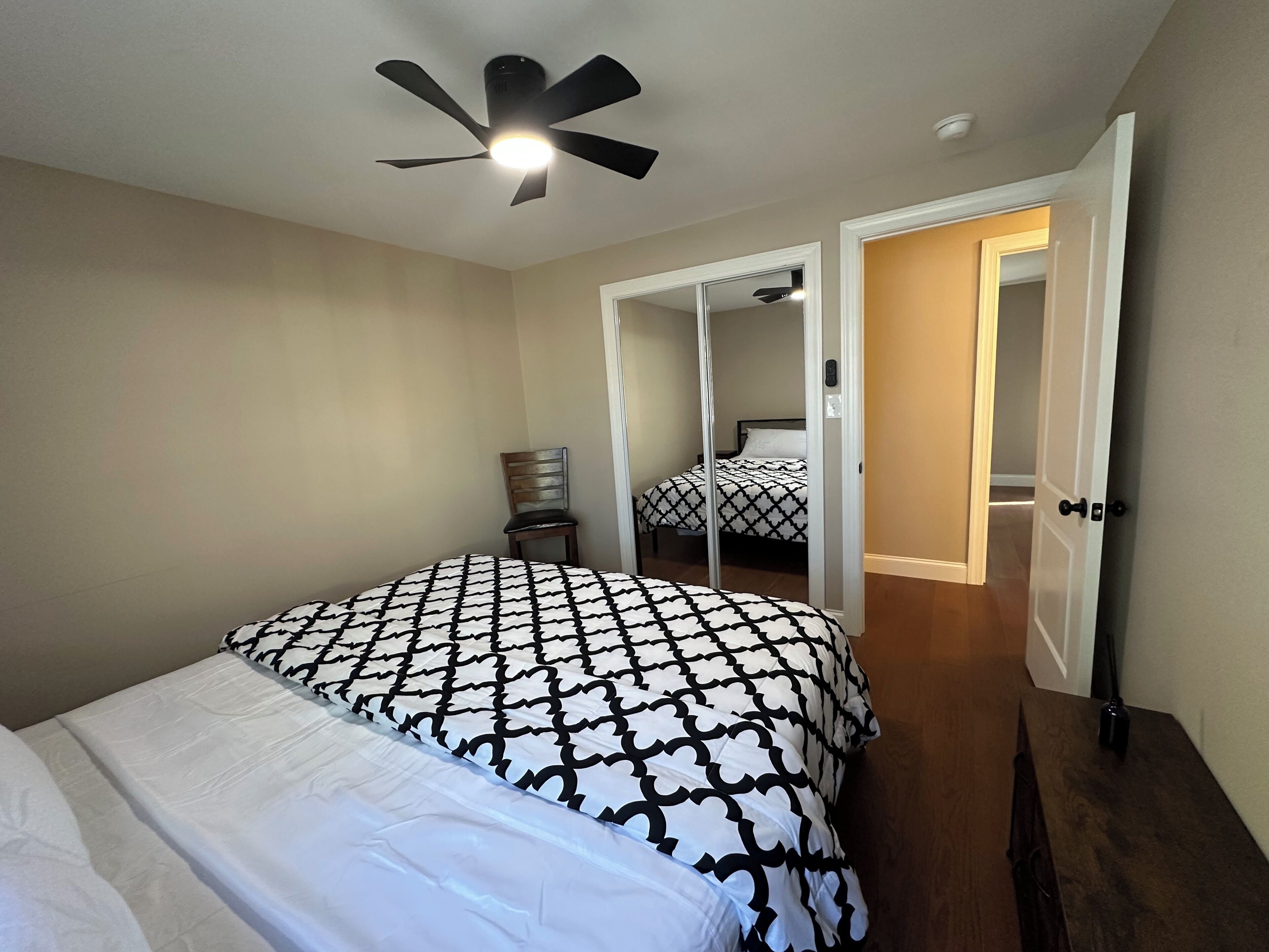 Une chambre à coucher comprenant un lit, une chaise, un ventilateur de plafond et une porte donnant sur une autre pièce.