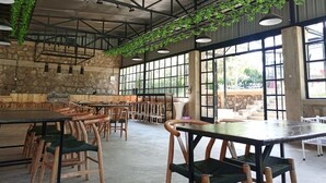 Un vaste espace intérieur doté de hauts plafonds, de grandes fenêtres et de plantes suspendues. Des tables et des chaises sont disposées pour permettre aux gens de s’asseoir.