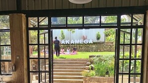 Een gevel met een grote glazen deur, een betonnen vloer en een bordje met de tekst 'TAKAMEGA'.