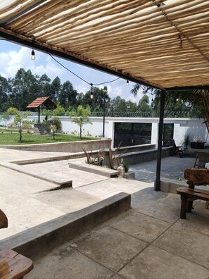 An outdoor patio area with a bamboo roof, stone flooring, and a view of a white building in the background. - Petrichor House Kakamega (Kakamega)