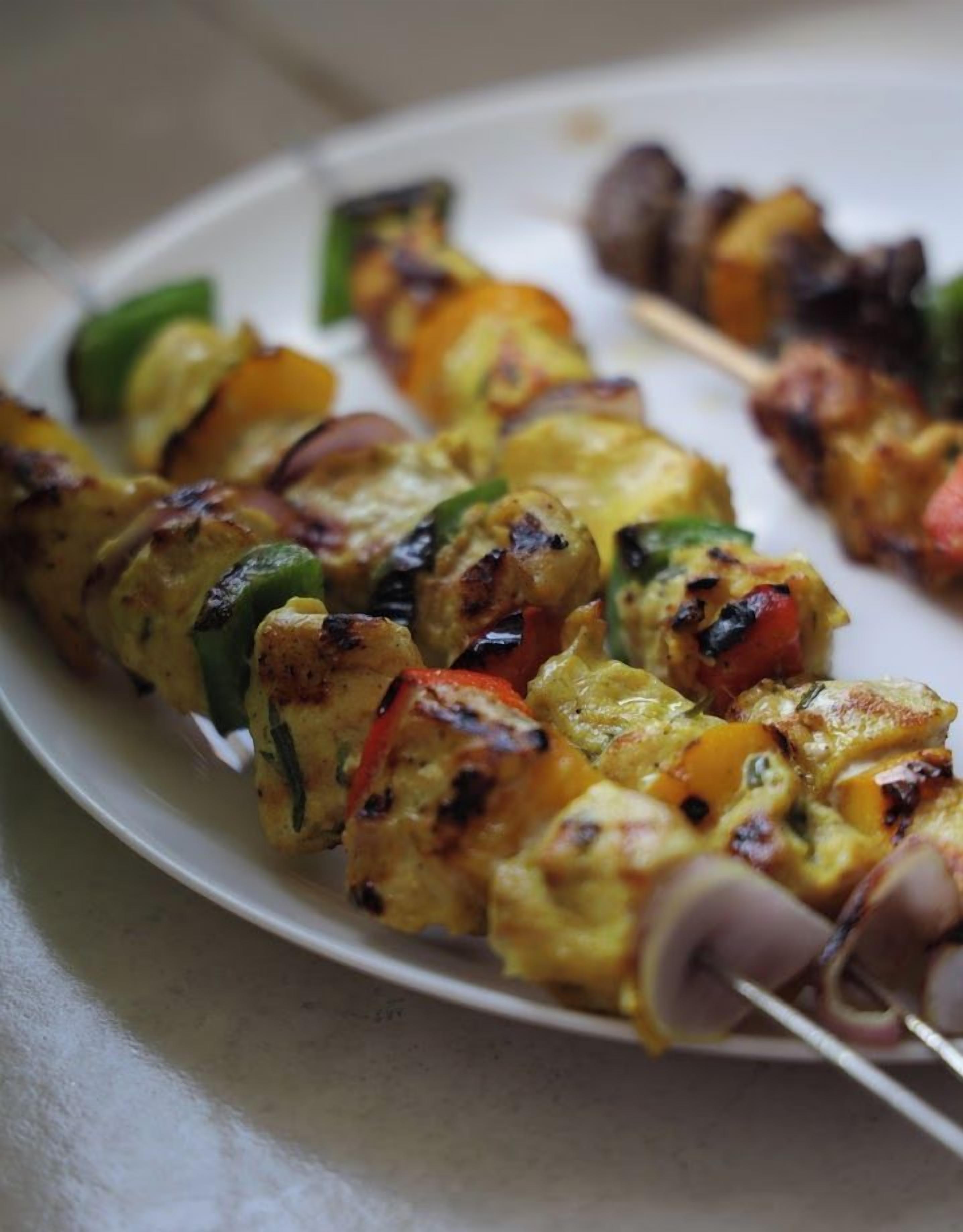 Un plato con brochetas de pollo y verduras a la parrilla.