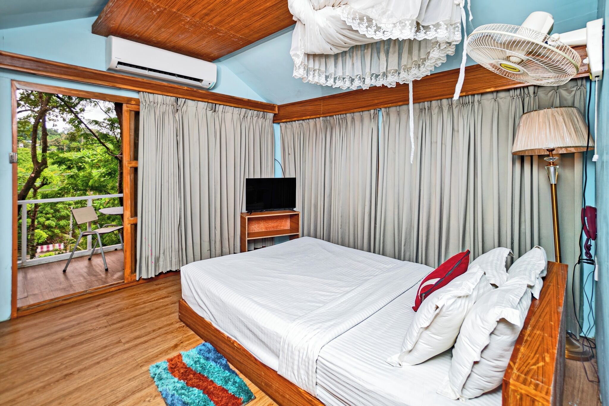 A bedroom with a bed, a TV, a fan, and a view of greenery outside.