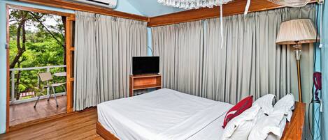 A bedroom with a bed, a TV, a fan, and a view of greenery outside.