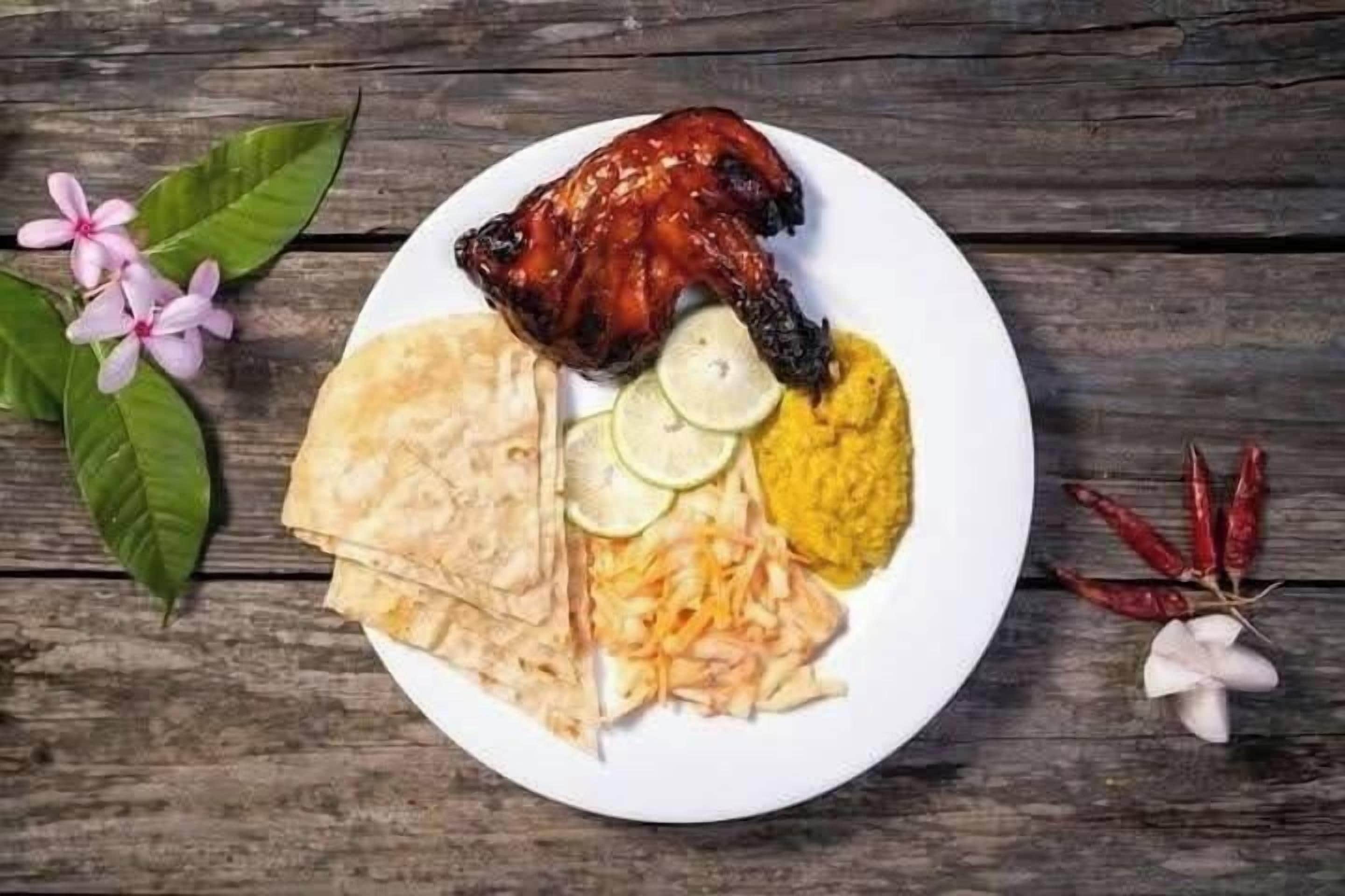 A plate with grilled chicken, flatbread, sliced cucumbers, and a yellow condiment, possibly curry, on a wooden table.