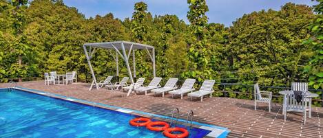 A swimming pool with lounge chairs and a covered seating area, surrounded by lush greenery.
