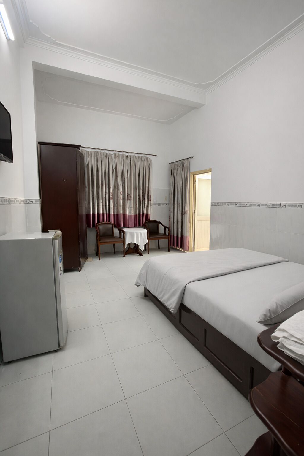 A hotel room with a bed, a desk, a chair, a table, a wardrobe, and a television.