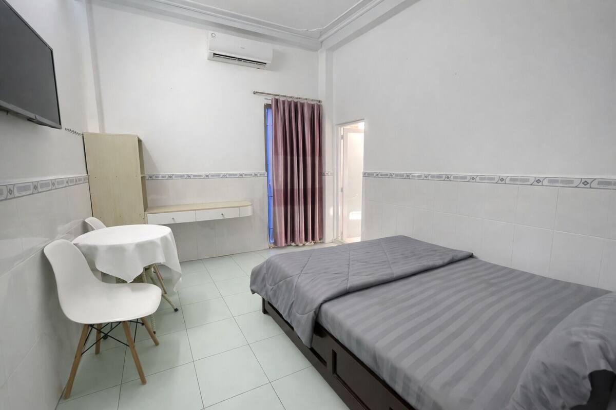 A room with a bed, a desk with a chair, a TV, and a window with curtains.