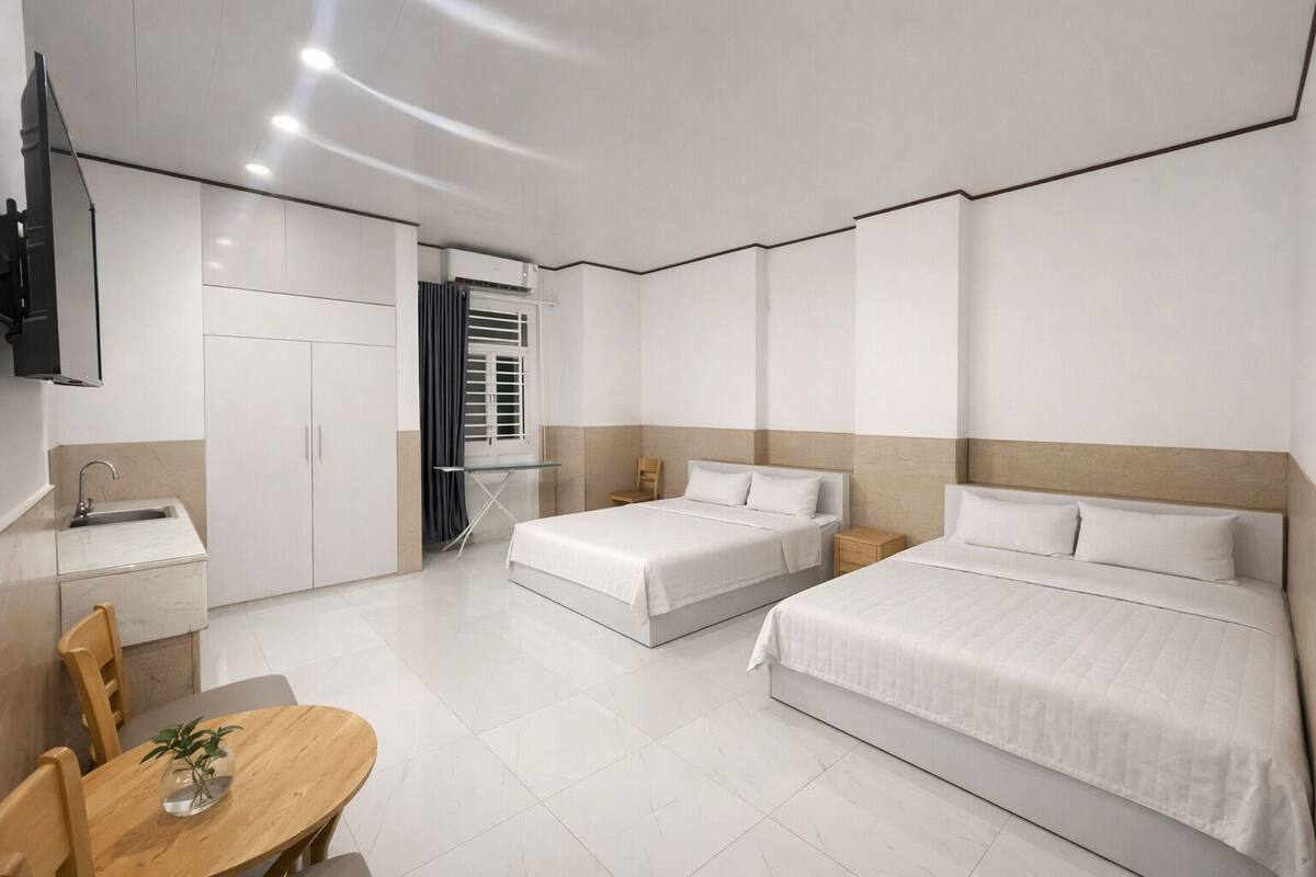 A hotel room with two beds, a desk, a chair, a TV, and a window with curtains.