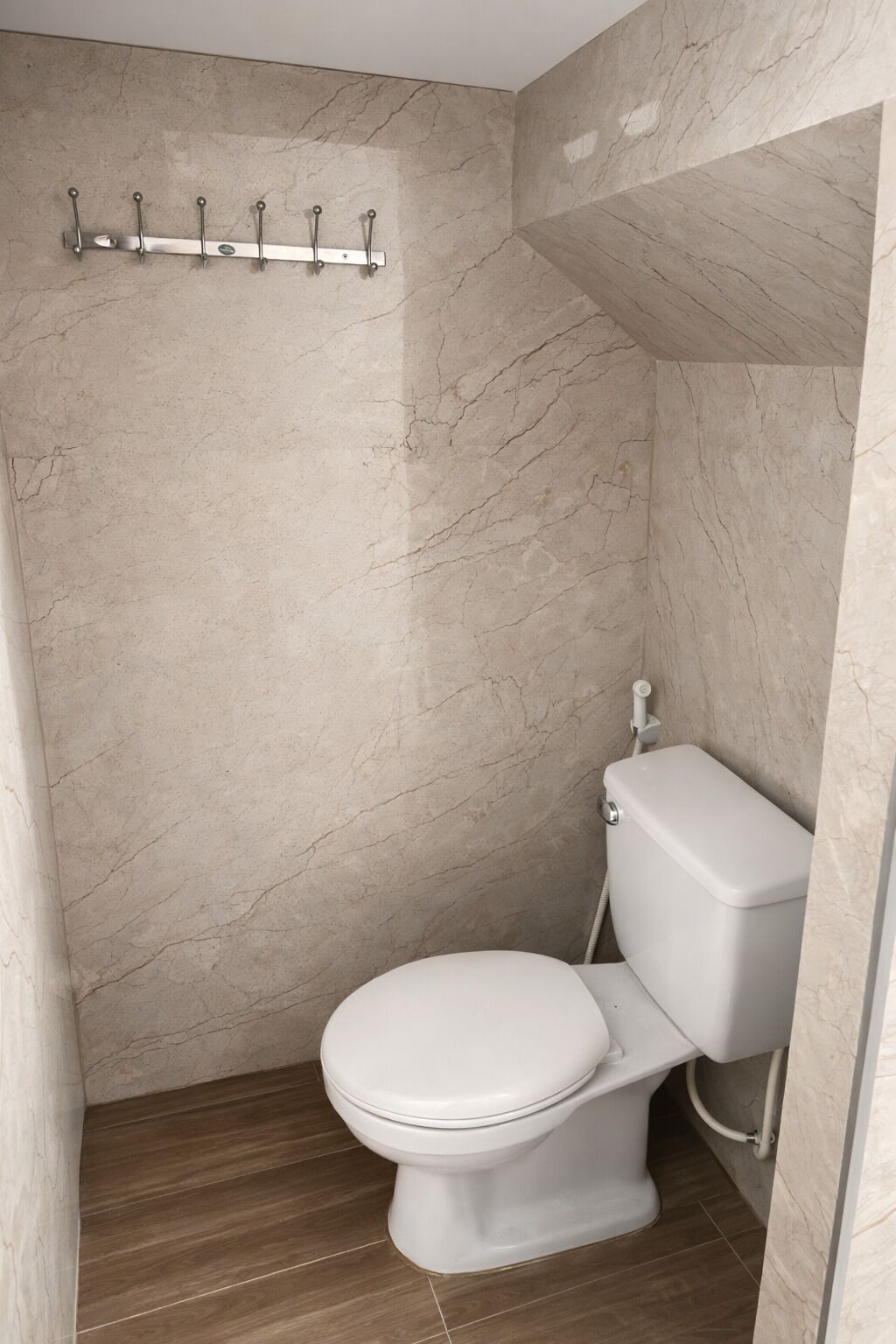 A bathroom with a marble wall, a white toilet, and a shower area.
