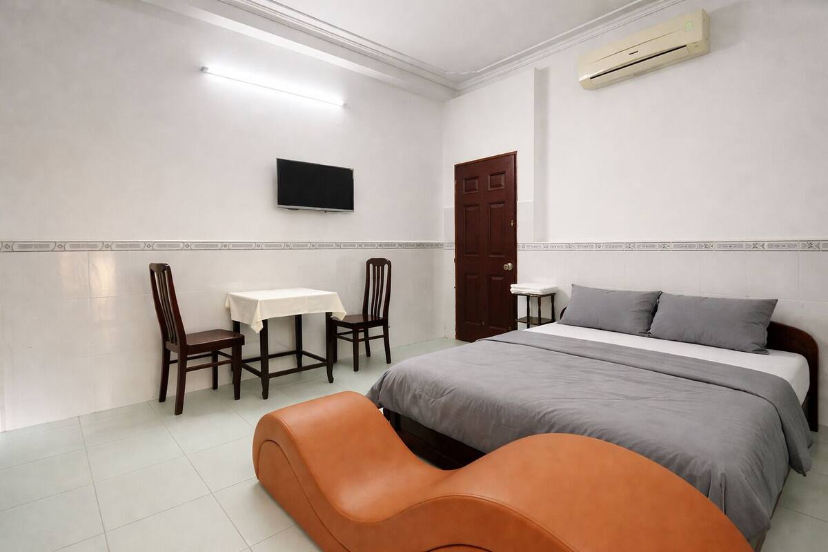 A bedroom with a bed, a desk, two chairs, a TV, and an air conditioner.