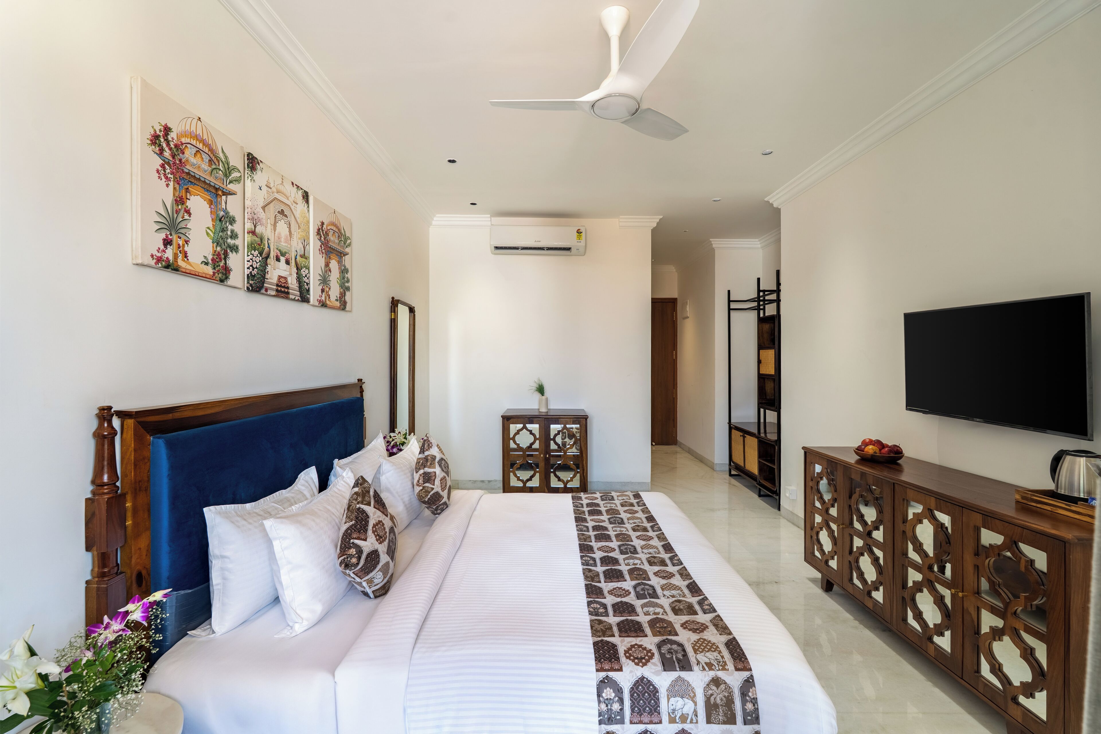 Une chambre d’hôtel avec un grand lit, une télévision, un ventilateur de plafond et des œuvres d’art accrochées au mur.