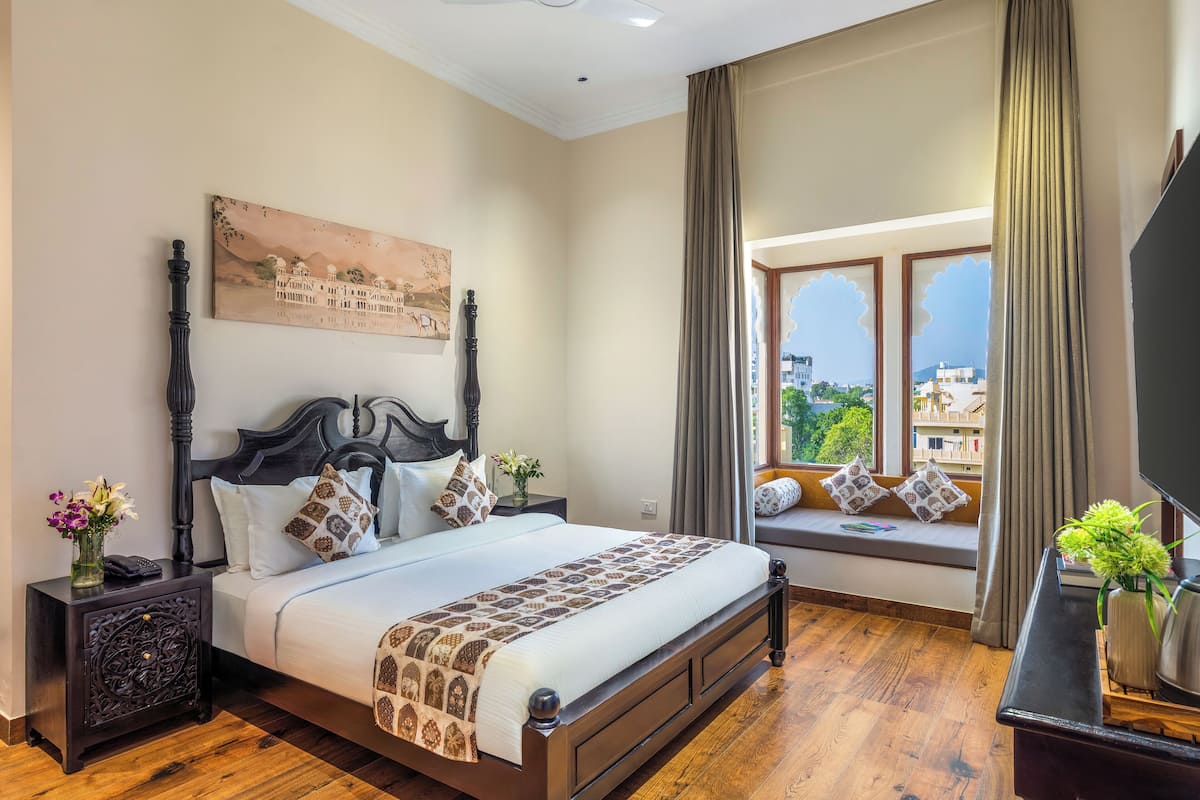 Een slaapkamer met een groot bed, een nachtkastje, een vensterbank met uitzicht, en een tv op een standaard.
