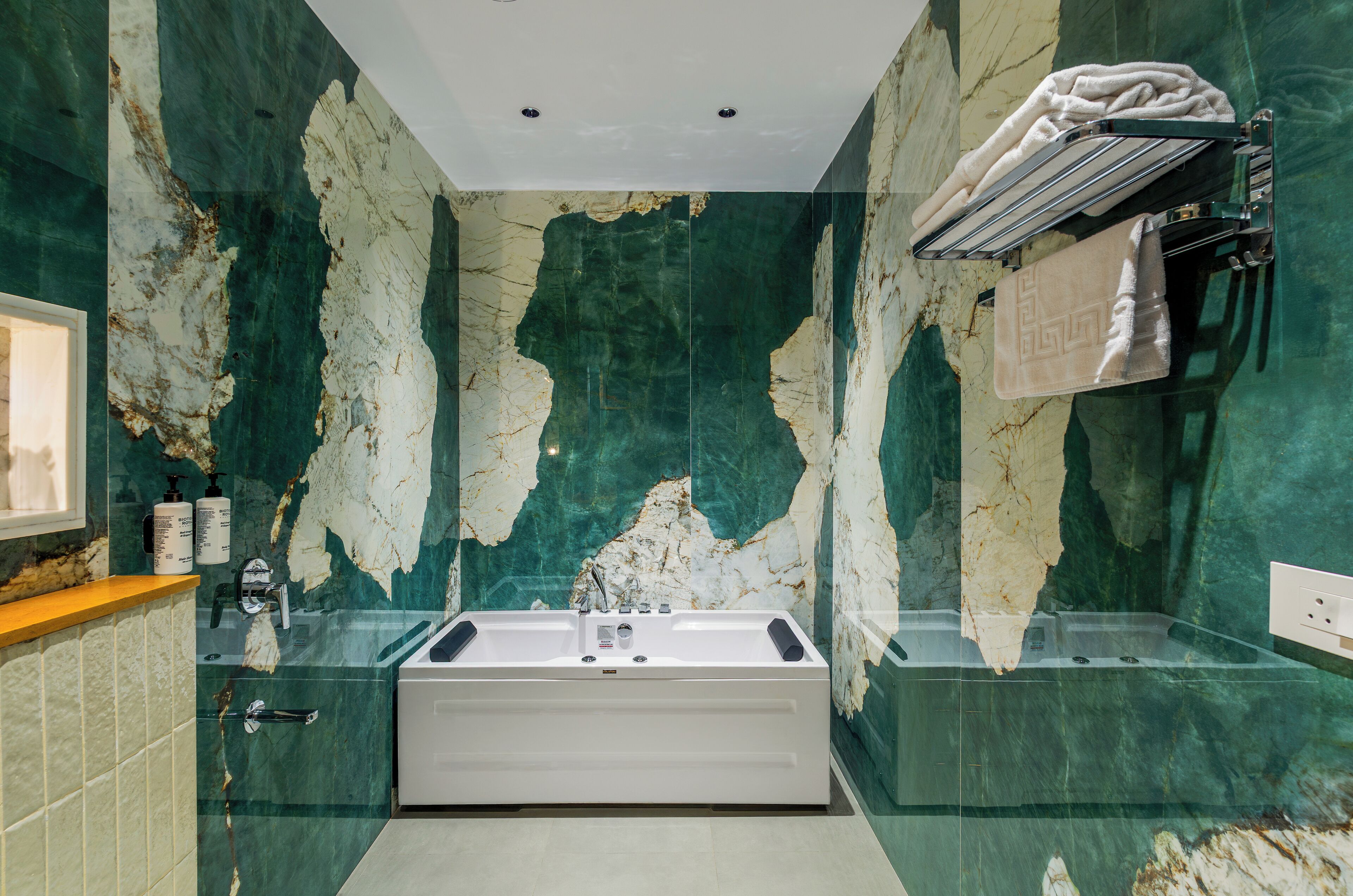 A bathroom with a large bathtub, marble walls, and a towel rack with towels.