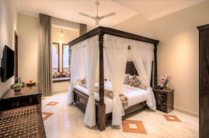 A four-poster bed with a canopy, a flat-screen TV, a bedside table with a vase of flowers, and a decorative rug. - The Classic Crown Udaipur - A Luxury Hotel by Lake Pichola (Udaipur)