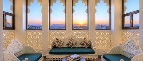 A room with a sofa set, a table, and three windows with decorative frames.