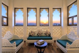 Habitación con sofá, una mesa y tres ventanas con detalles decorativos.