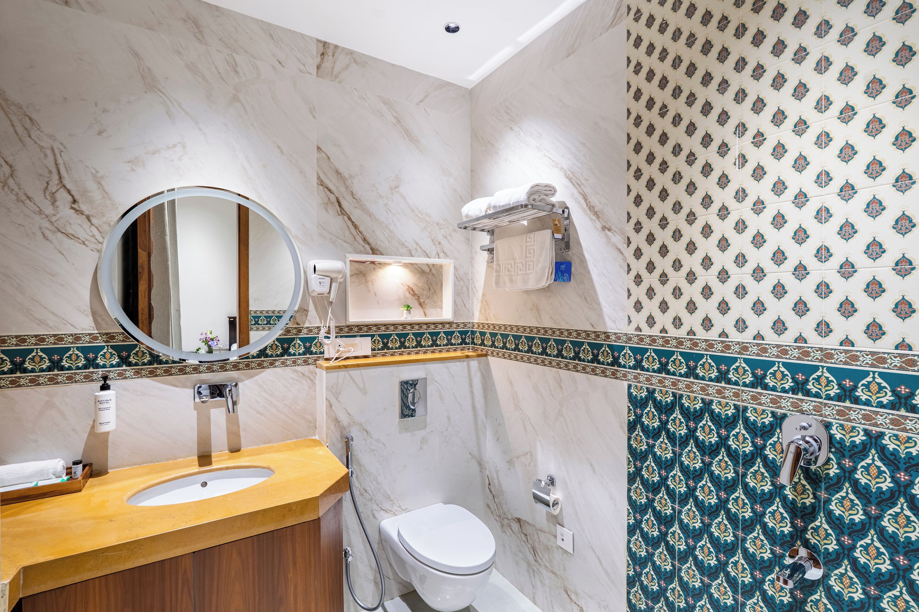 A bathroom with a marble vanity, a round mirror, a toilet, and a shower area with patterned tiles.