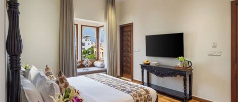 A bedroom with a four-poster bed, a television on a wooden console table, and a window with a view of buildings.