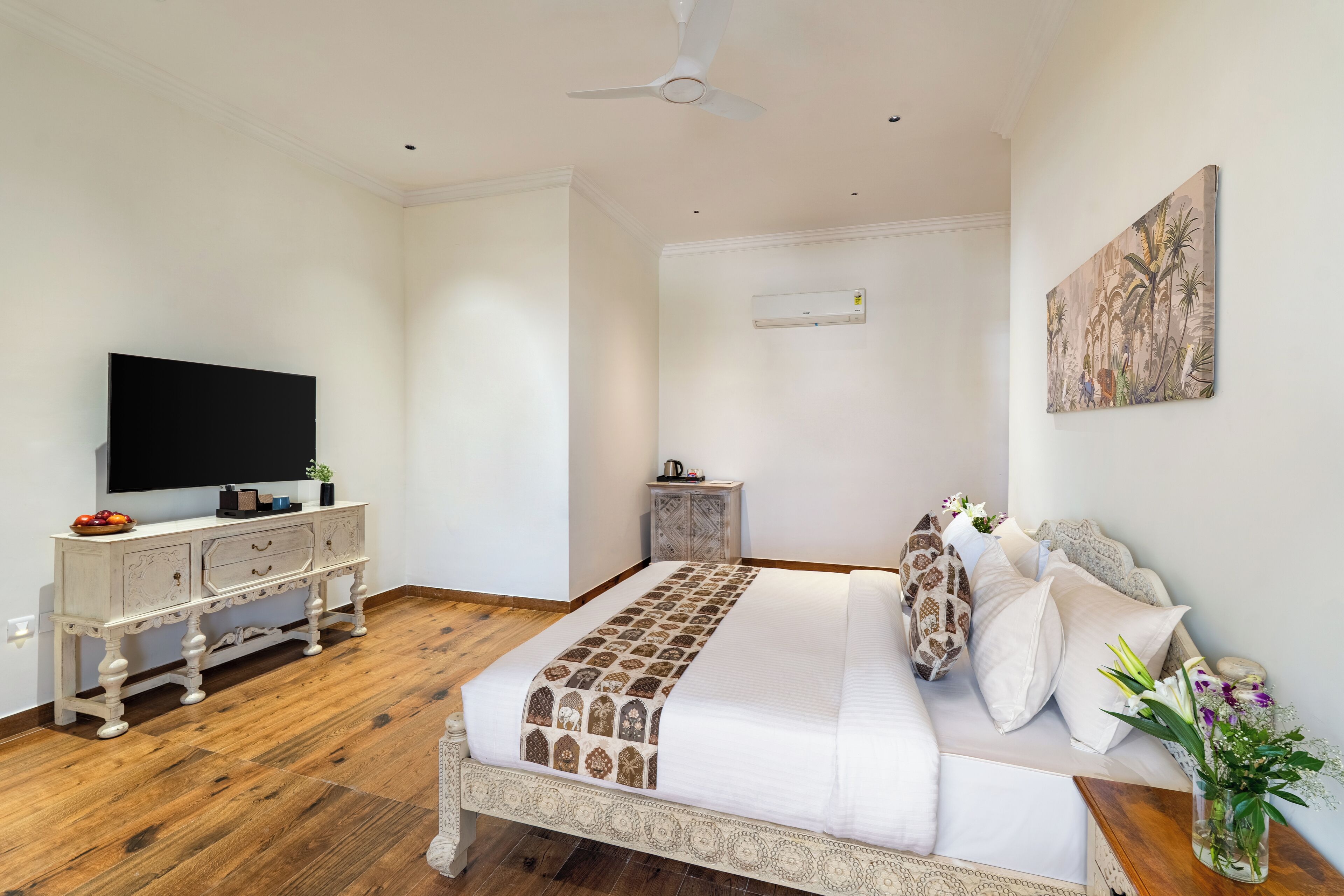 A bedroom with a large bed, a TV, a ceiling fan, and a painting on the wall.