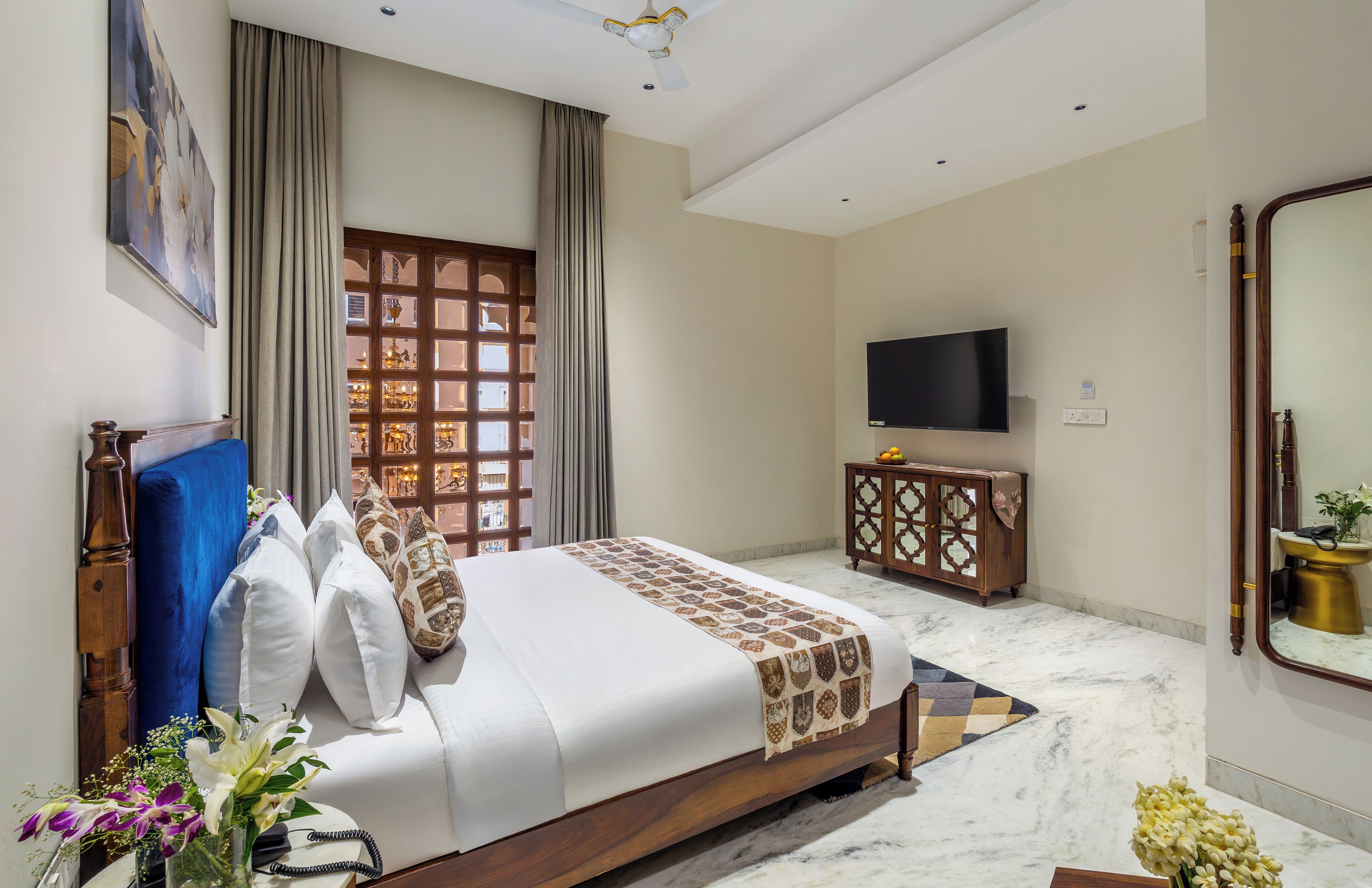 A bedroom with a bed, a TV, a mirror, and a window with curtains.