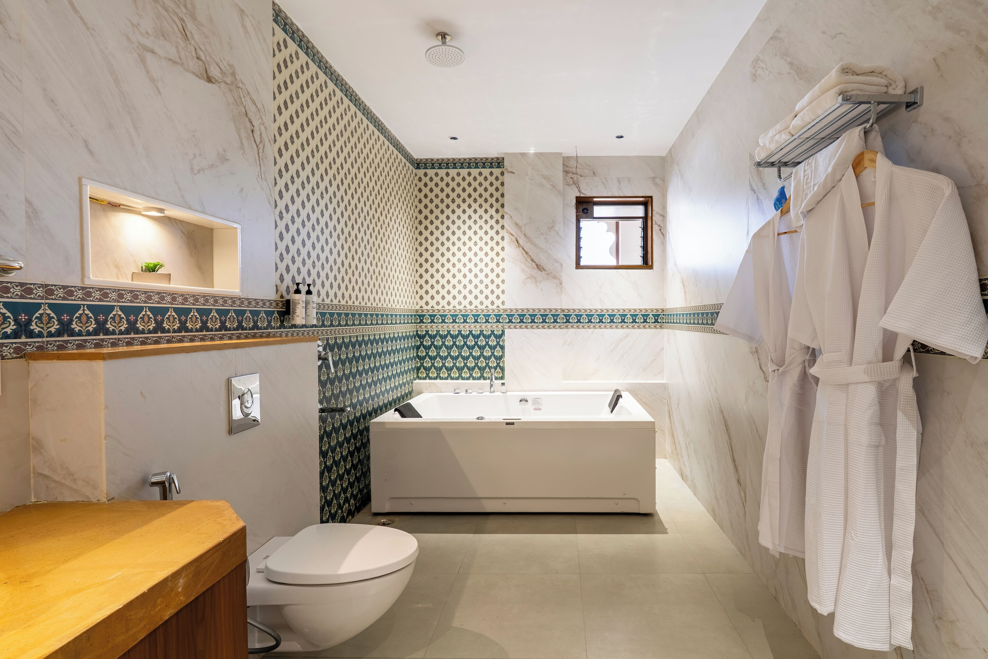 Ein modernes Badezimmer mit Marmor-Waschtisch, freistehender Badewanne und Handtuchhalter mit Bademänteln.