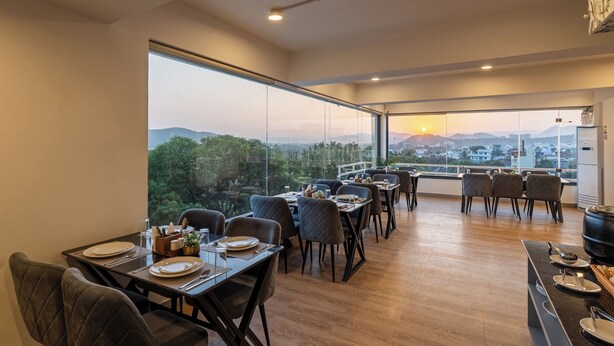 Uma sala de jantar com mesas preparadas para dois, amplas janelas com vista para a cidade e design de interiores moderno.