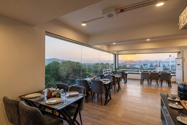 A dining area with tables set for two, large windows offering a city view, and a modern interior design. - The Classic Crown Udaipur - A Luxury Hotel by Lake Pichola (Udaipur)