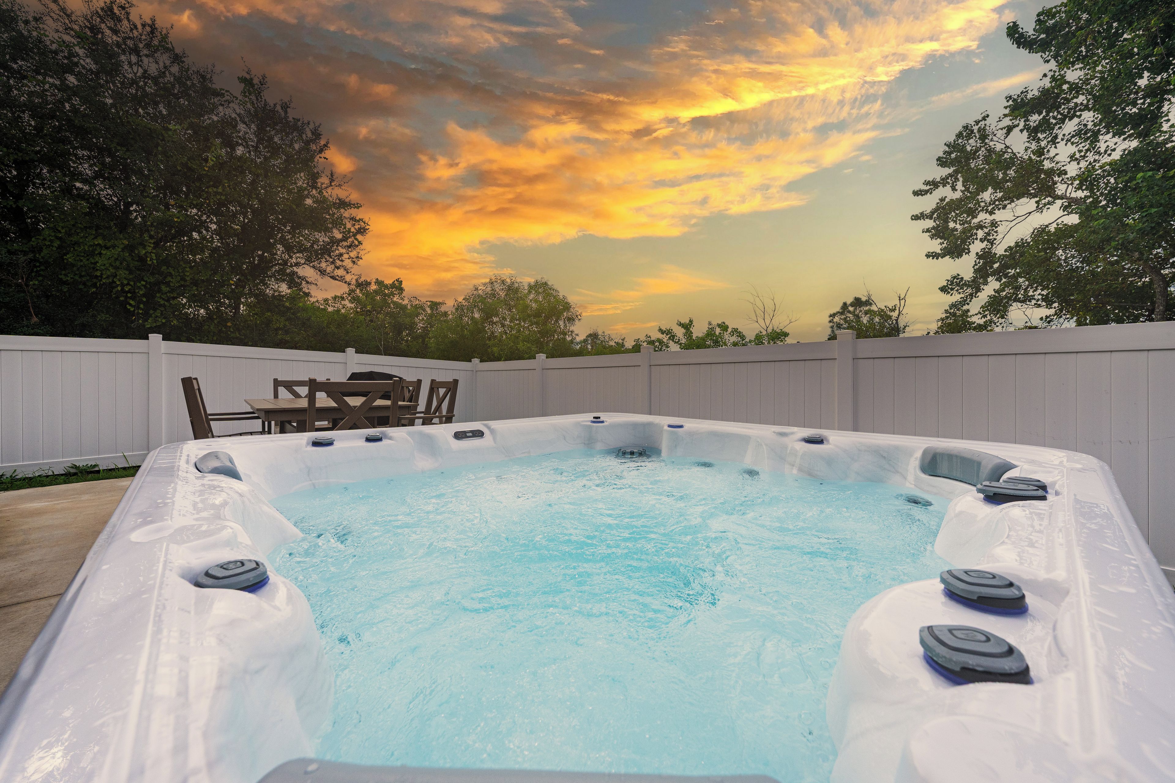 A hot tub with a wooden deck and a white fence in the background.