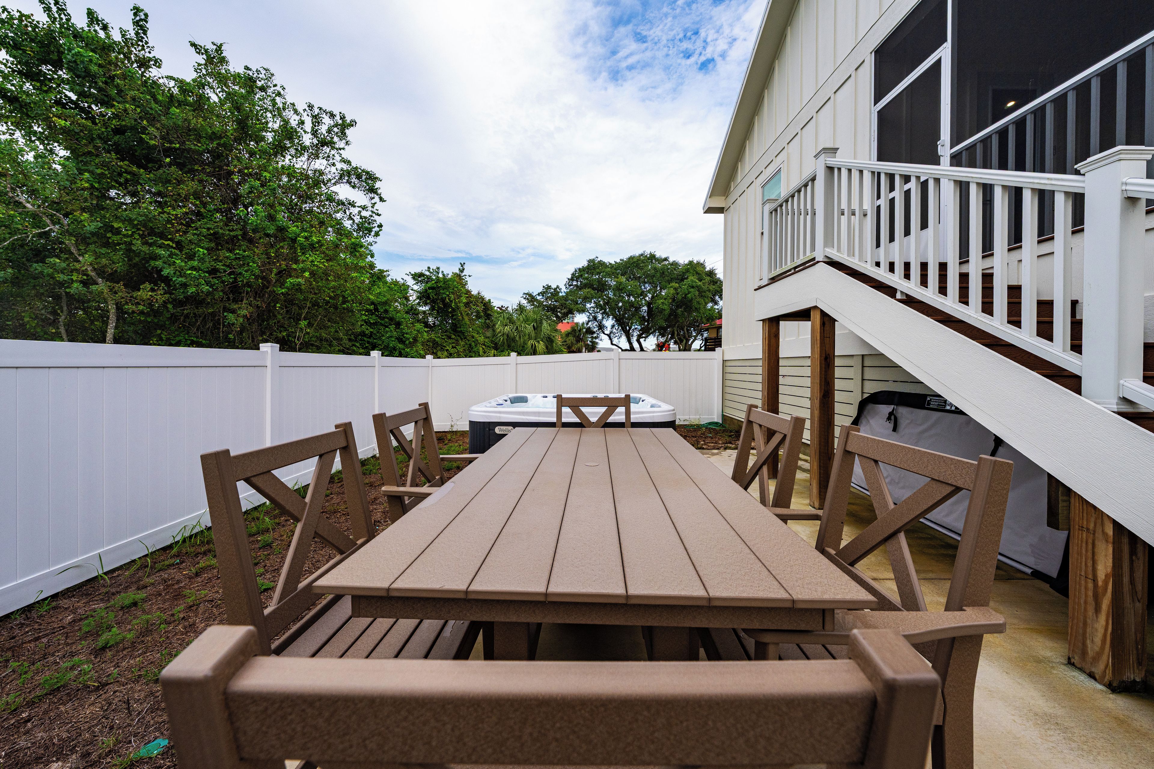 A wooden deck with a table and chairs, a hot tub, and a white fence.
