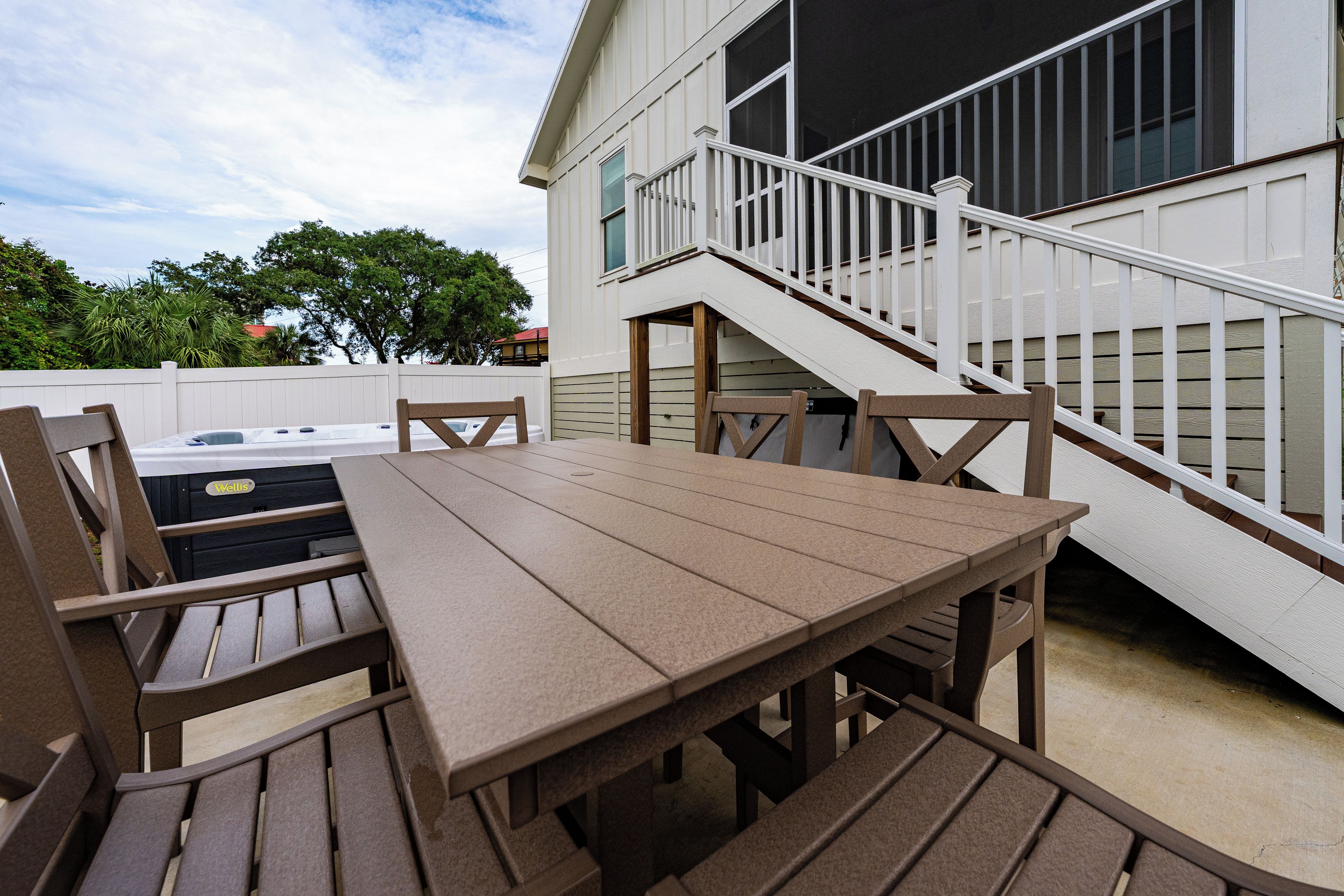 An outdoor patio with a wooden table and chairs, a covered seating area, and a staircase leading to a balcony.