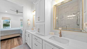 A modern bathroom with a large mirror, white cabinetry, and a shower area.