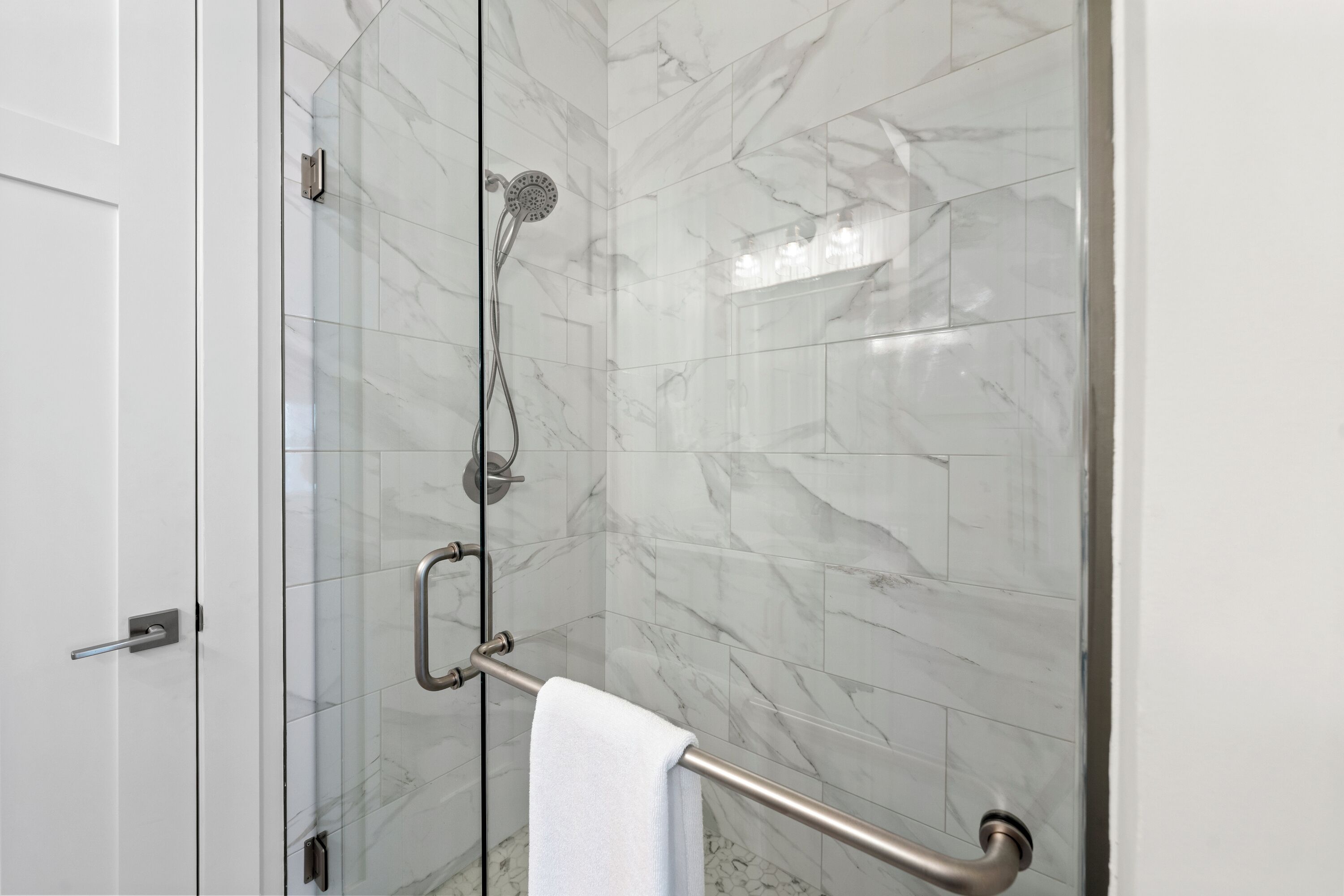 A modern bathroom with a glass shower enclosure, marble tiles, and a towel rack.