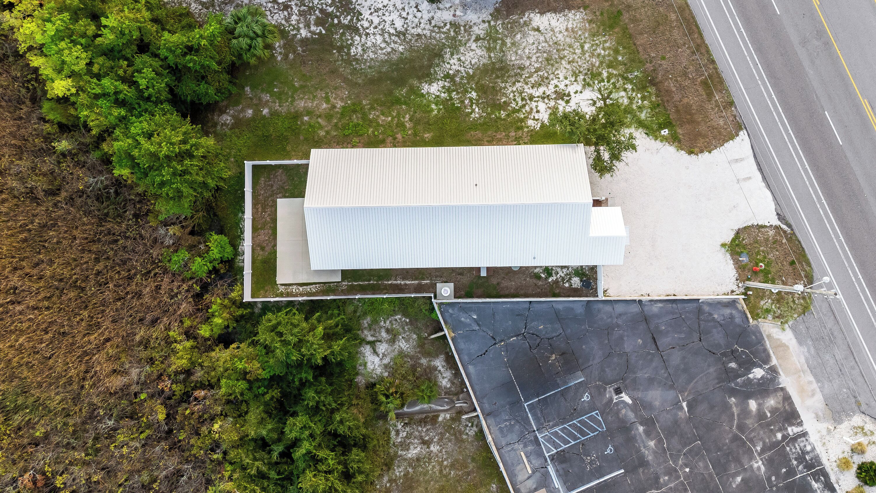 An aerial view of a building with a flat roof, surrounded by dense greenery and a parking area with visible parking lines and a disabled parking space.