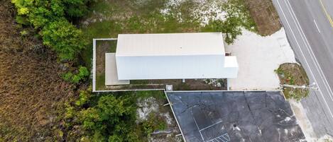 An aerial view of a building with a flat roof, surrounded by dense greenery and a parking area with visible parking lines and a disabled parking space.