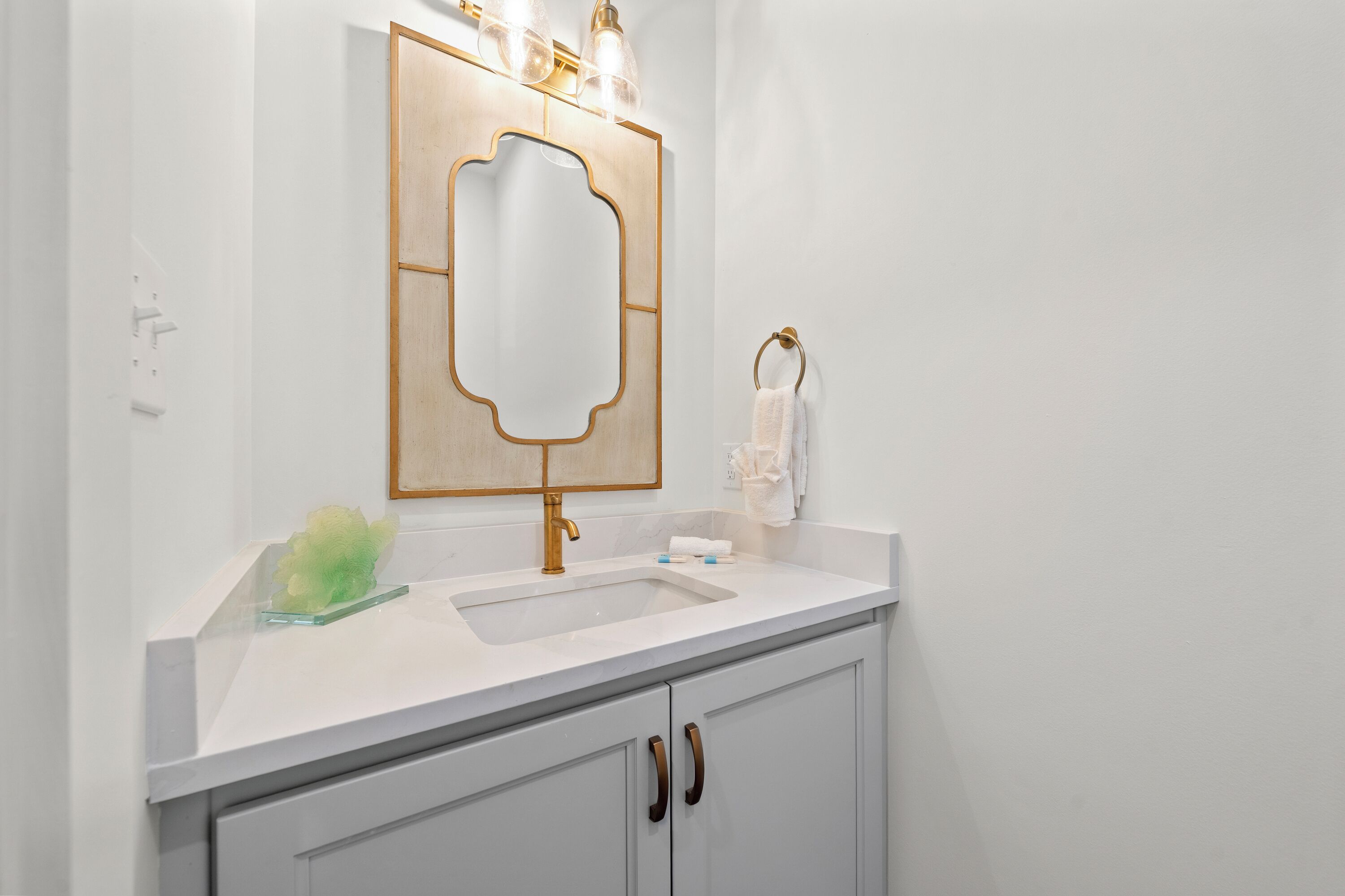 A bathroom with a white sink, a gold faucet, and a mirror with a gold frame.
