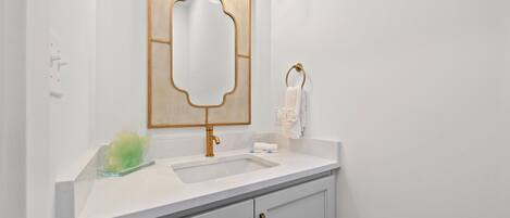Une salle de bain avec un lavabo blanc, un robinet doré et un miroir avec un cadre doré.