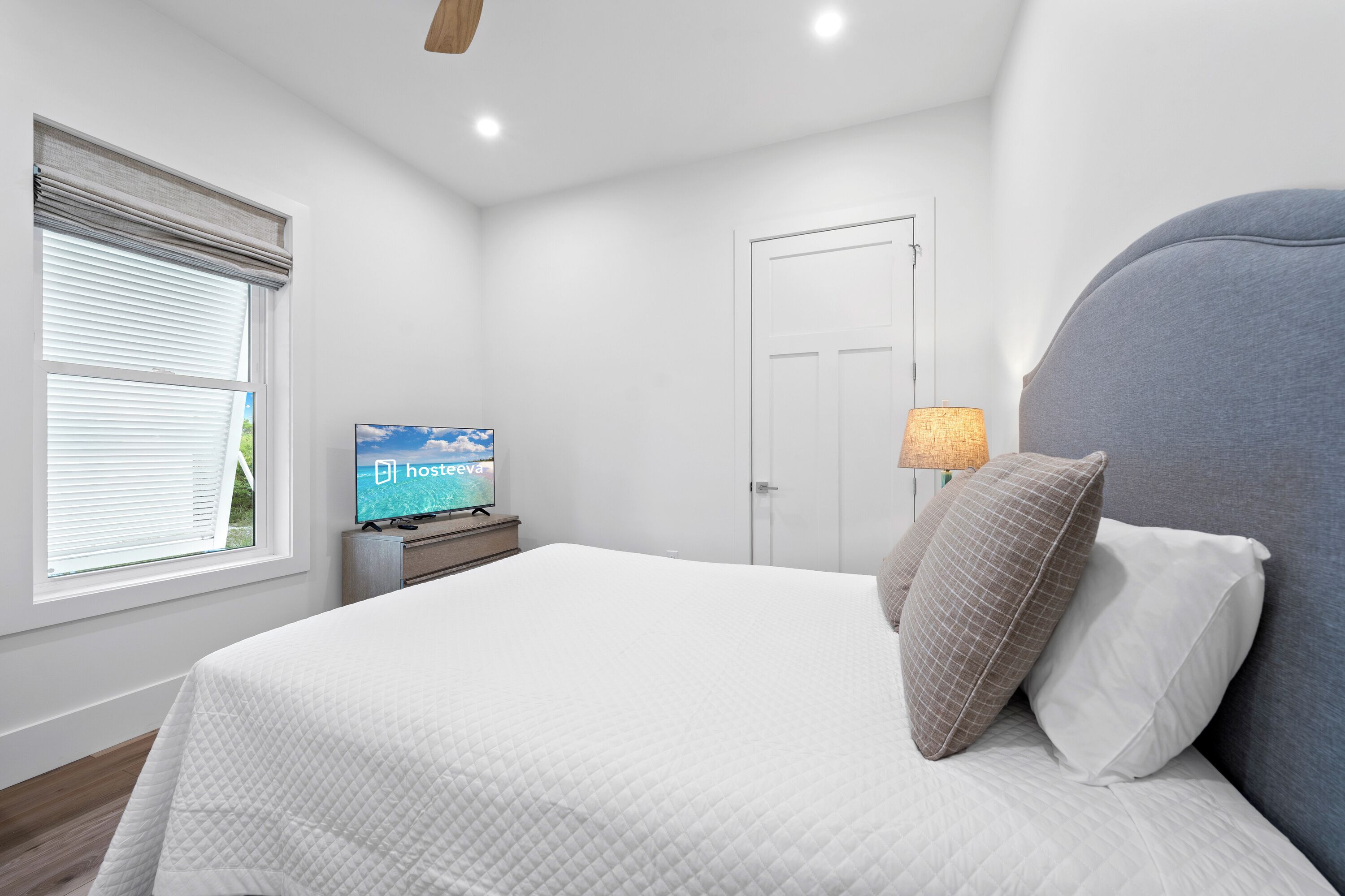 A bedroom with a bed, a television, a door, and a window with blinds.